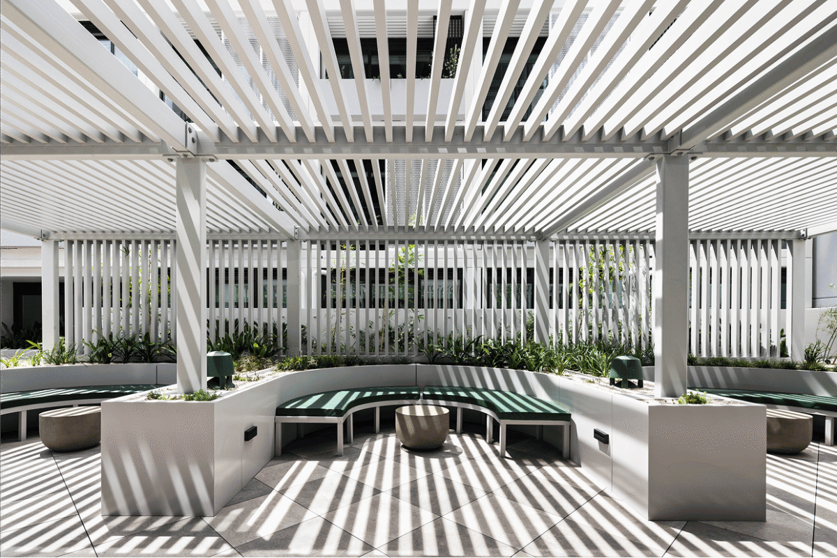 Contemporary outdoor courtyard with linear white pergola, curved green seating and sculptural shadows — a refined, architectural space styled by BOWERBIRD Interiors.