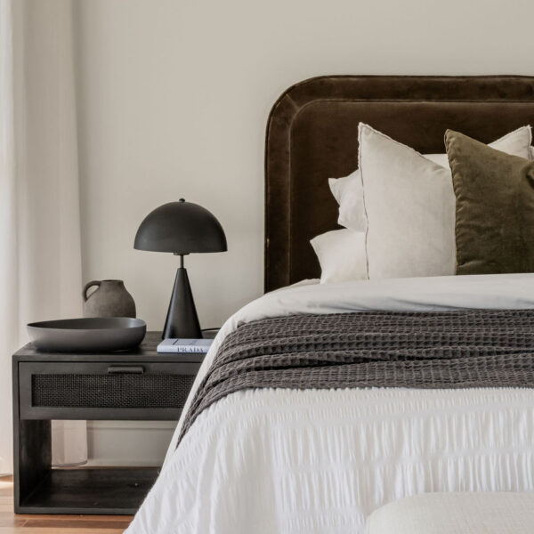 Stylish Bedroom With a Brown Upholstered Headboard, White Bedding, Green Throw Pillows, and a Black Bedside Table With a Modern Lamp