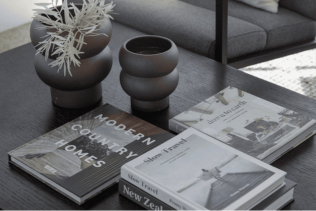 Close-up of a black coffee table in a commercial lounge, styled with stacked design and travel books, two matte black ceramic vases, and dried foliage.