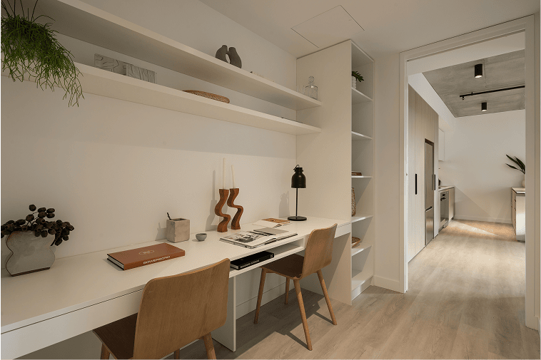 Modern Sydney home office styled by BOWERBIRD Interiors with minimalist shelving, warm timber chairs, and soft lighting leading to a contemporary kitchen.